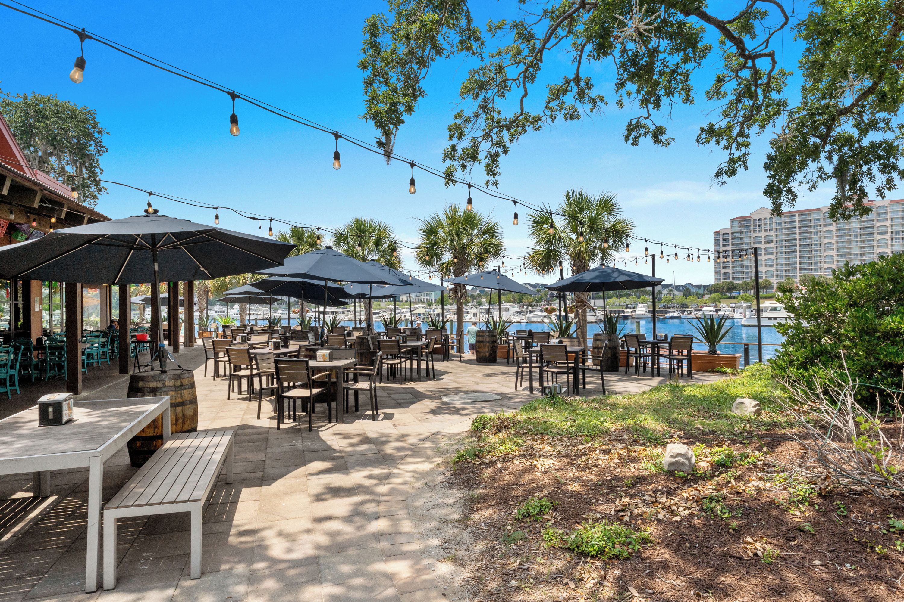 An outdoor dining area with tables and umbrellas, overlooking a marina with boats.