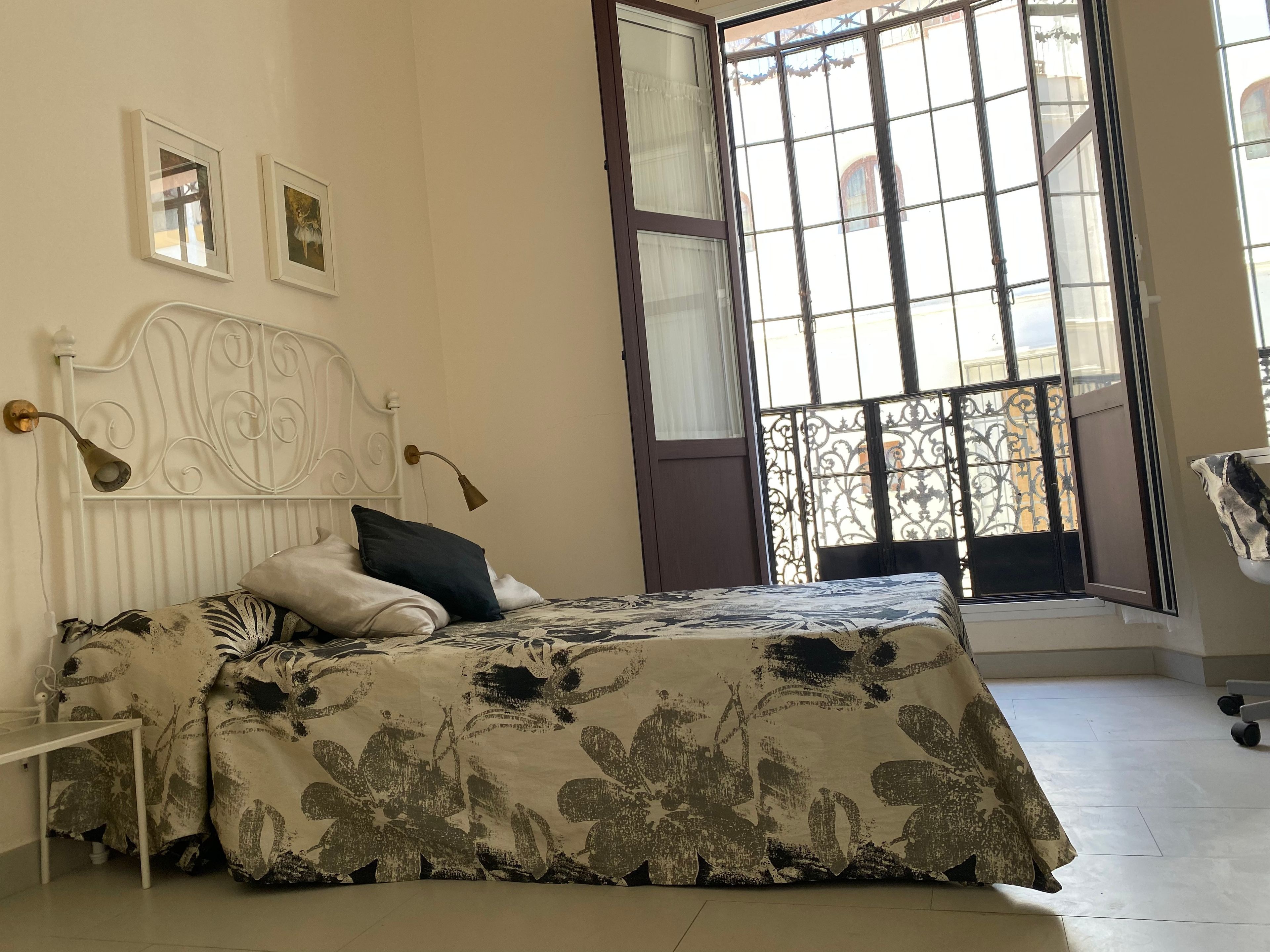 Un dormitorio con cama, mesita de noche, lámpara y ventana con vistas a edificios.