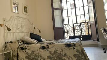 Un dormitorio con cama, mesita de noche, lámpara y ventana con vistas a edificios.