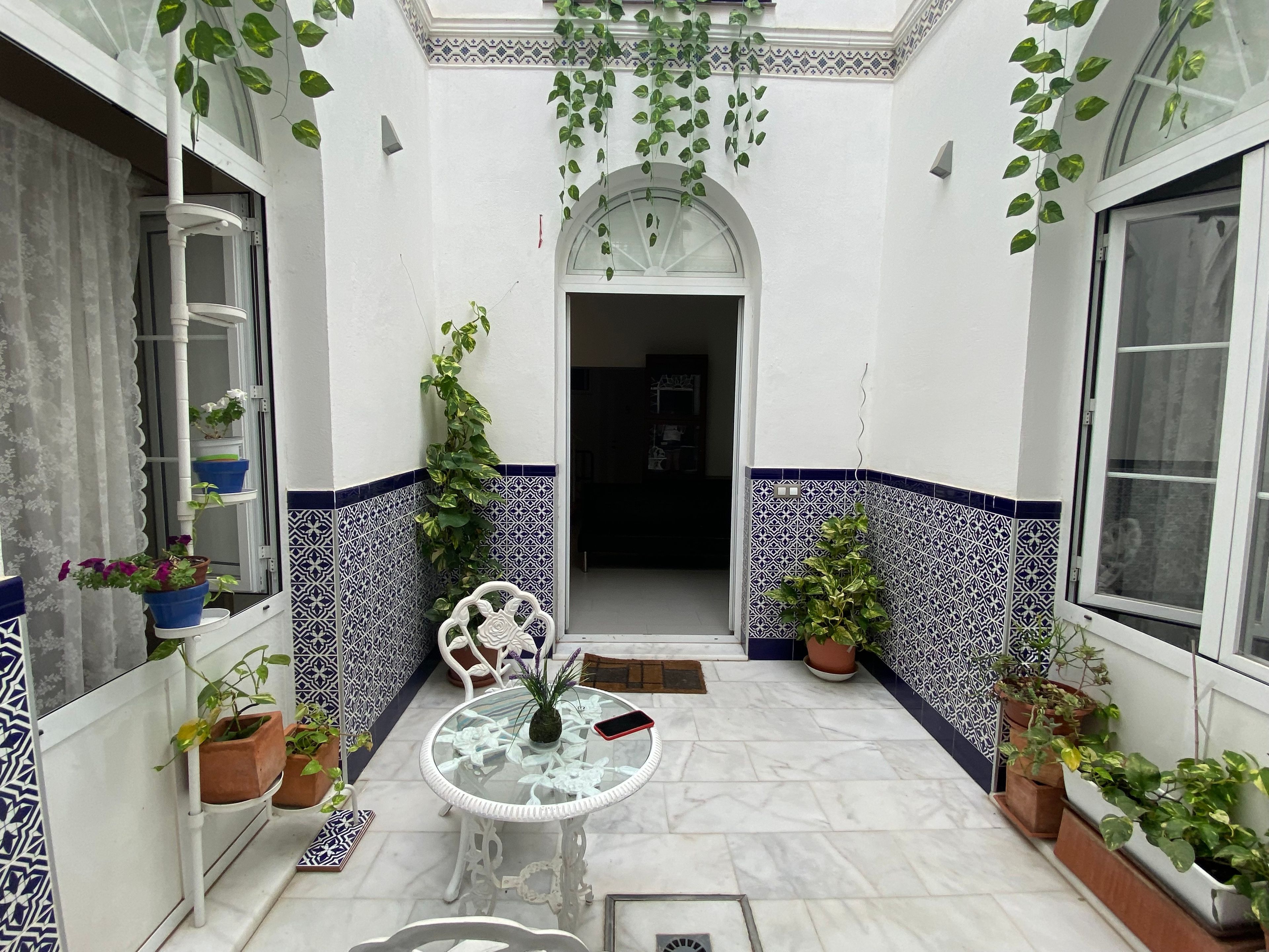 Un pequeño patio amurallado con suelo de baldosas, una mesa de cristal y plantas en macetas.