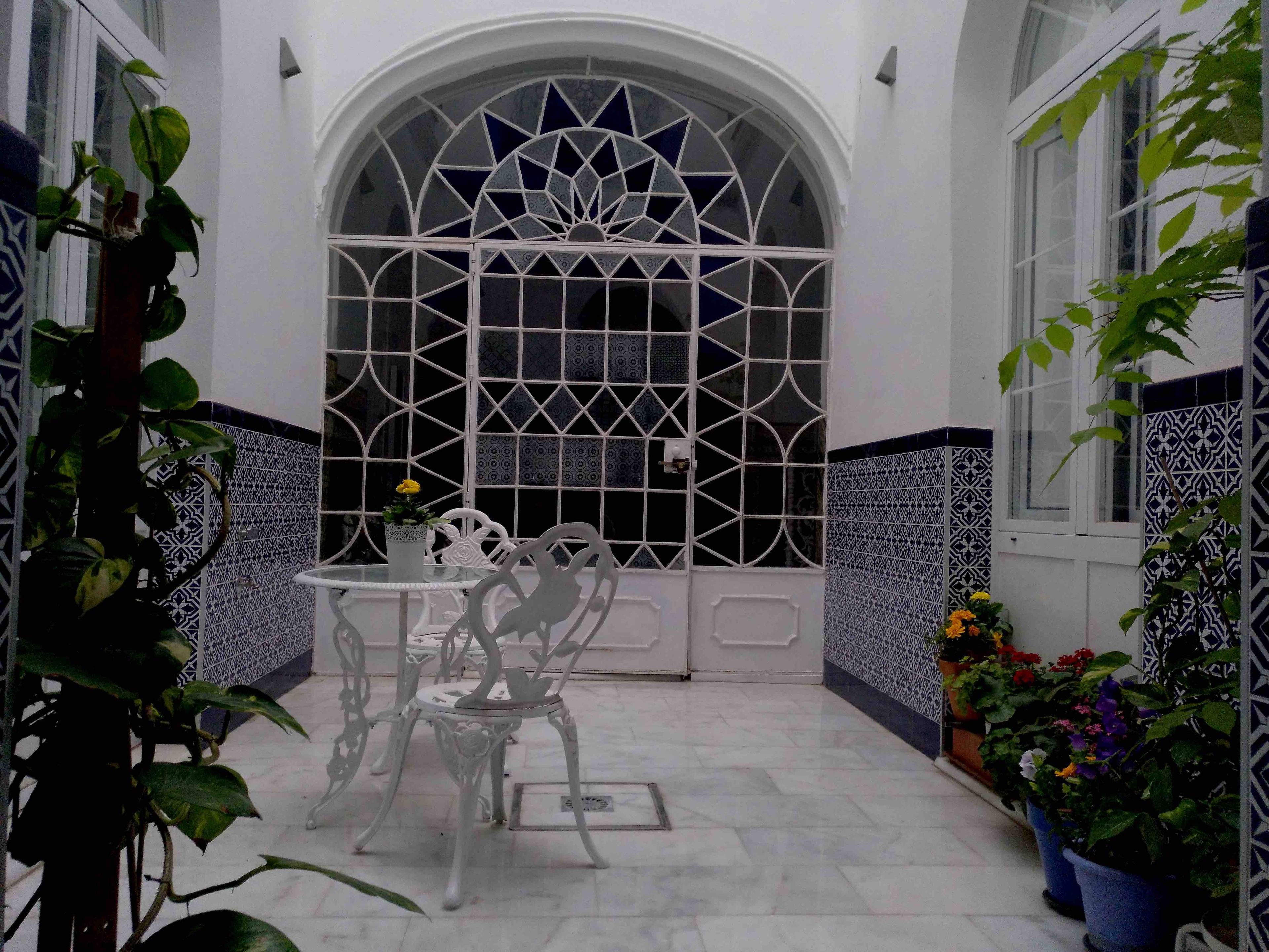 Un patio con un ventanal arqueado blanco, una mesa con sillas y plantas en macetas.