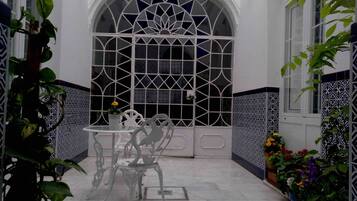 Un patio con un ventanal arqueado blanco, una mesa con sillas y plantas en macetas.