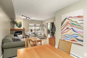 Een moderne woonkamer met een open haard, een eethoek met een houten tafel, en een groot abstract schilderij aan de muur.