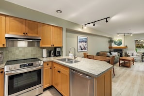 A modern kitchen with wooden cabinets, stainless steel appliances, and a granite countertop. - Walk to Creekside Gondola – Cozy 1BR Condo w/ Patio, Pool & Hot Tub Access (Whistler)