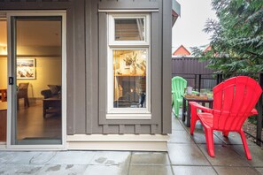 A residential exterior with a sliding glass door, a window, and a patio area with two chairs. - Walk to Creekside Gondola – Cozy 1BR Condo w/ Patio, Pool & Hot Tub Access (Whistler)