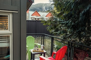 Een balkon met uitzicht op huizen, een rode stoel, een groene stoel en een tafel met een dienblad eten en drinken.