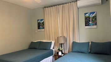 A hotel room with two single beds, a ceiling fan, an air conditioning unit, a lamp, and two wall-mounted pictures.
