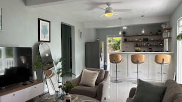 Een moderne woonkamer met een flatscreen televisie, een salontafel, een bank en een eethoek met barstoelen.