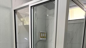 A glass-enclosed shower with a white tiled wall, a showerhead, and a soap dispenser. - Castaways Haven Apt, Few steps from Mero Beach (Mero)