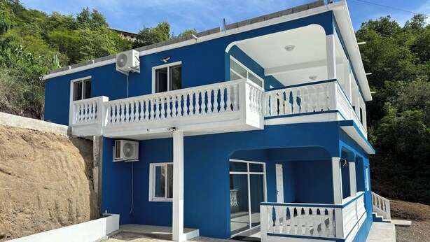 A two-story building with a balcony and a ground-level entrance. - Castaways Haven Apt, Few steps from Mero Beach (Mero)