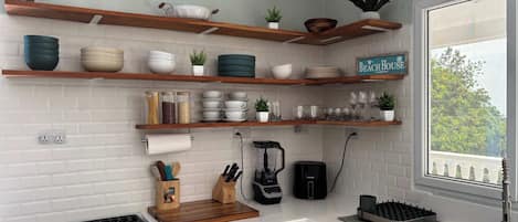 A kitchen with white cabinets, a gas stove, a coffee maker, and various kitchenware on wooden shelves.