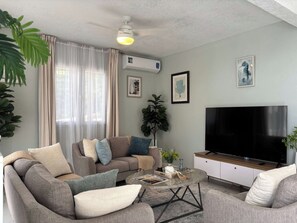 Ein Wohnzimmer mit einer Sofagarnitur, einem Couchtisch, einem Fernseher und einem Deckenventilator.