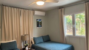 A bedroom with two beds, a ceiling fan, a window with curtains, and a wall-mounted air conditioner. - Castaways Haven Apt, Few steps from Mero Beach (Mero)