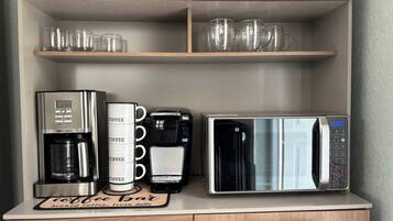 A kitchenette with a coffee maker, a coffee mug holder, and a microwave.