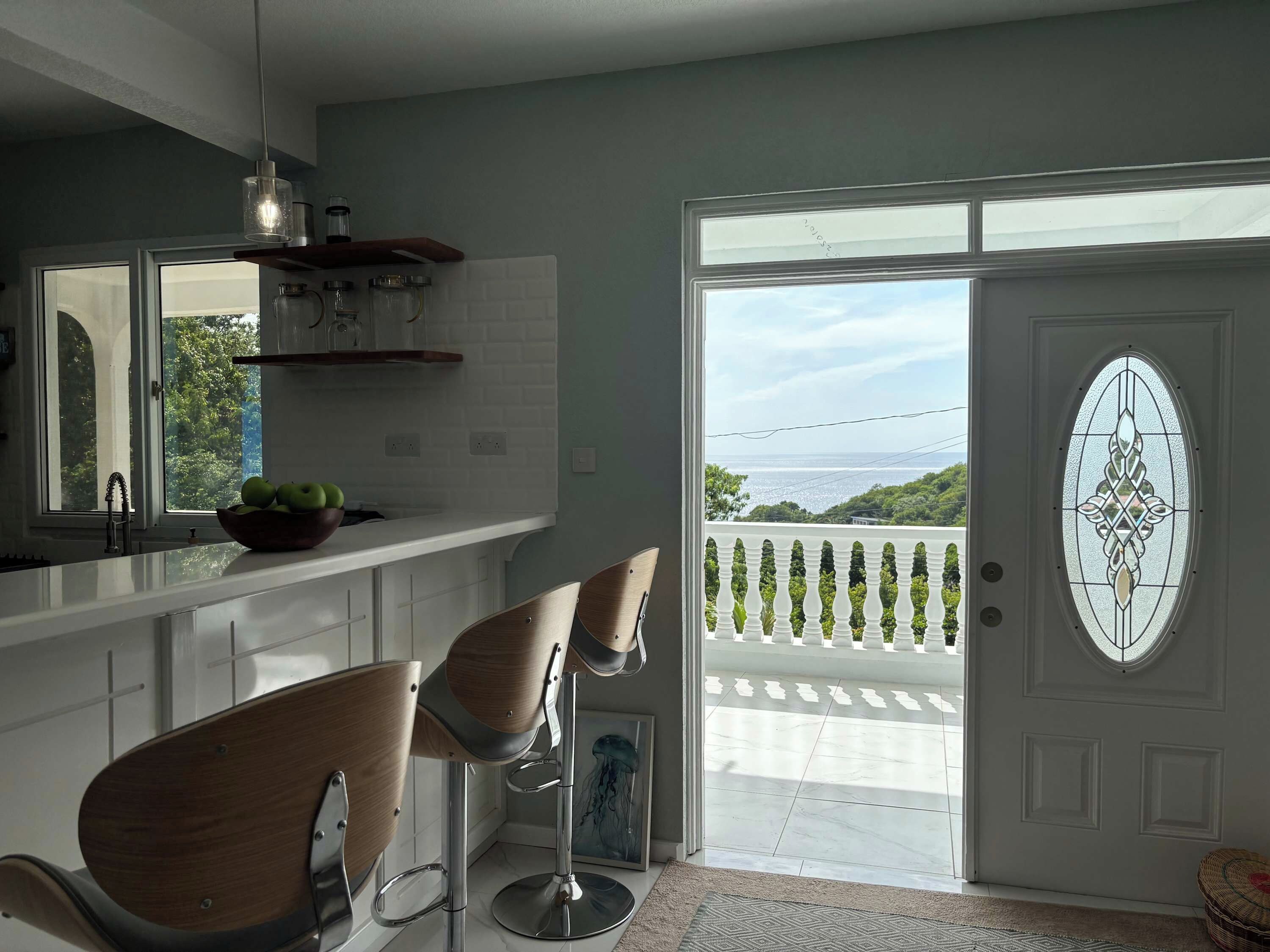 Una cucina moderna con un'ampia finestra, due sgabelli da bar e una porta decorativa vista mare.