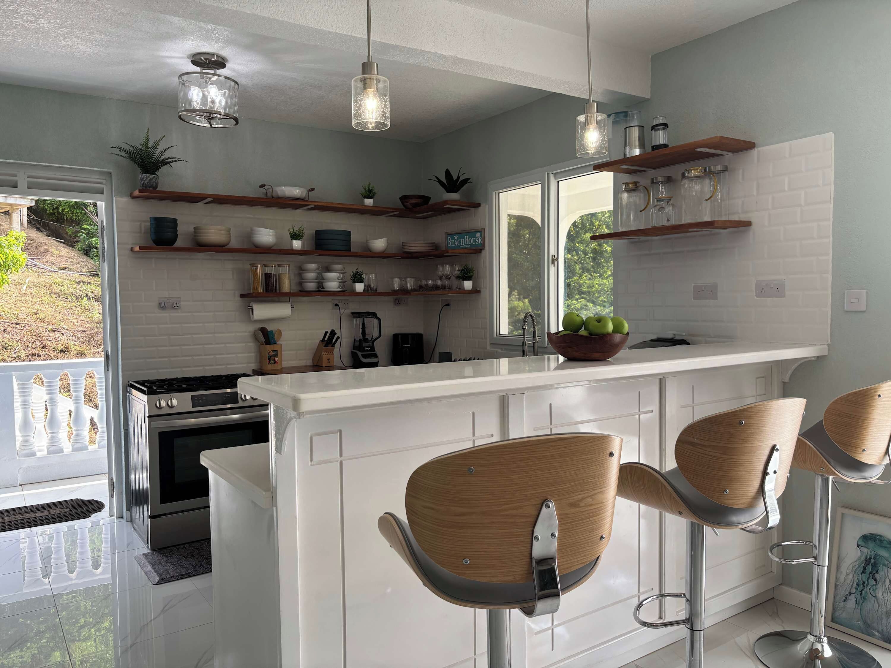A modern kitchen with white cabinetry, a central island with bar stools, pendant lighting, and a view of the outdoors.