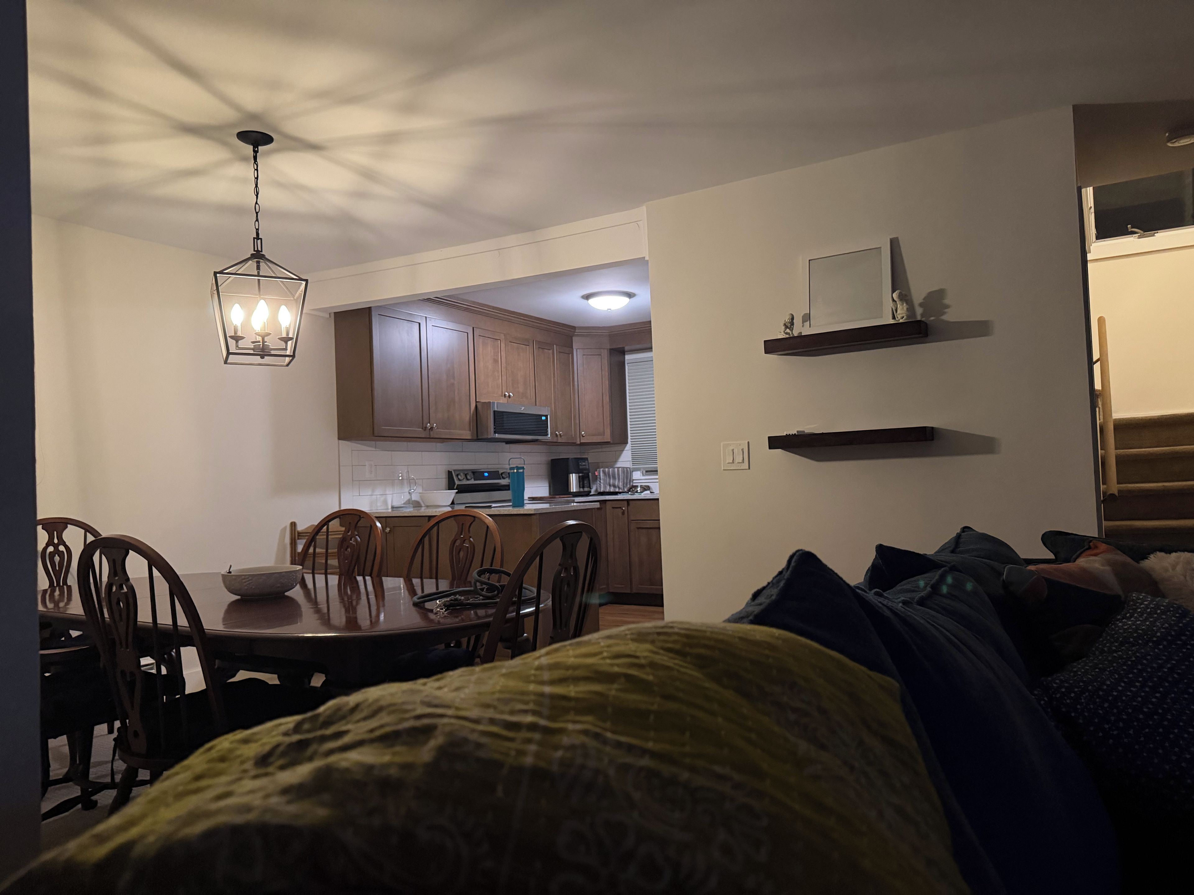 A compact living space with a dining area, kitchenette, and a bed with a green patterned blanket.