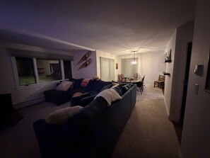 A living room with a dark-colored sofa, a dining table with chairs, and a hallway leading to a door. - Nestled on Haystack Mountain and golf course, just 5 miles from Mount Snow! (Wilmington)