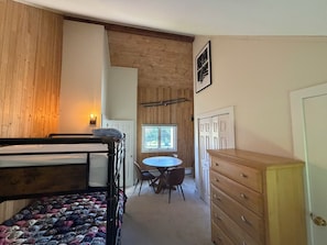 A room with bunk beds, a wooden dresser, a round table, and a window with a view. - Nestled on Haystack Mountain and golf course, just 5 miles from Mount Snow! (Wilmington)