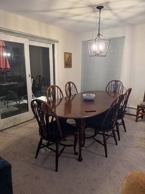 A dining area with a round table, six chairs, a chandelier, a painting, and a sliding glass door leading outside. - Nestled on Haystack Mountain and golf course, just 5 miles from Mount Snow! (Wilmington)