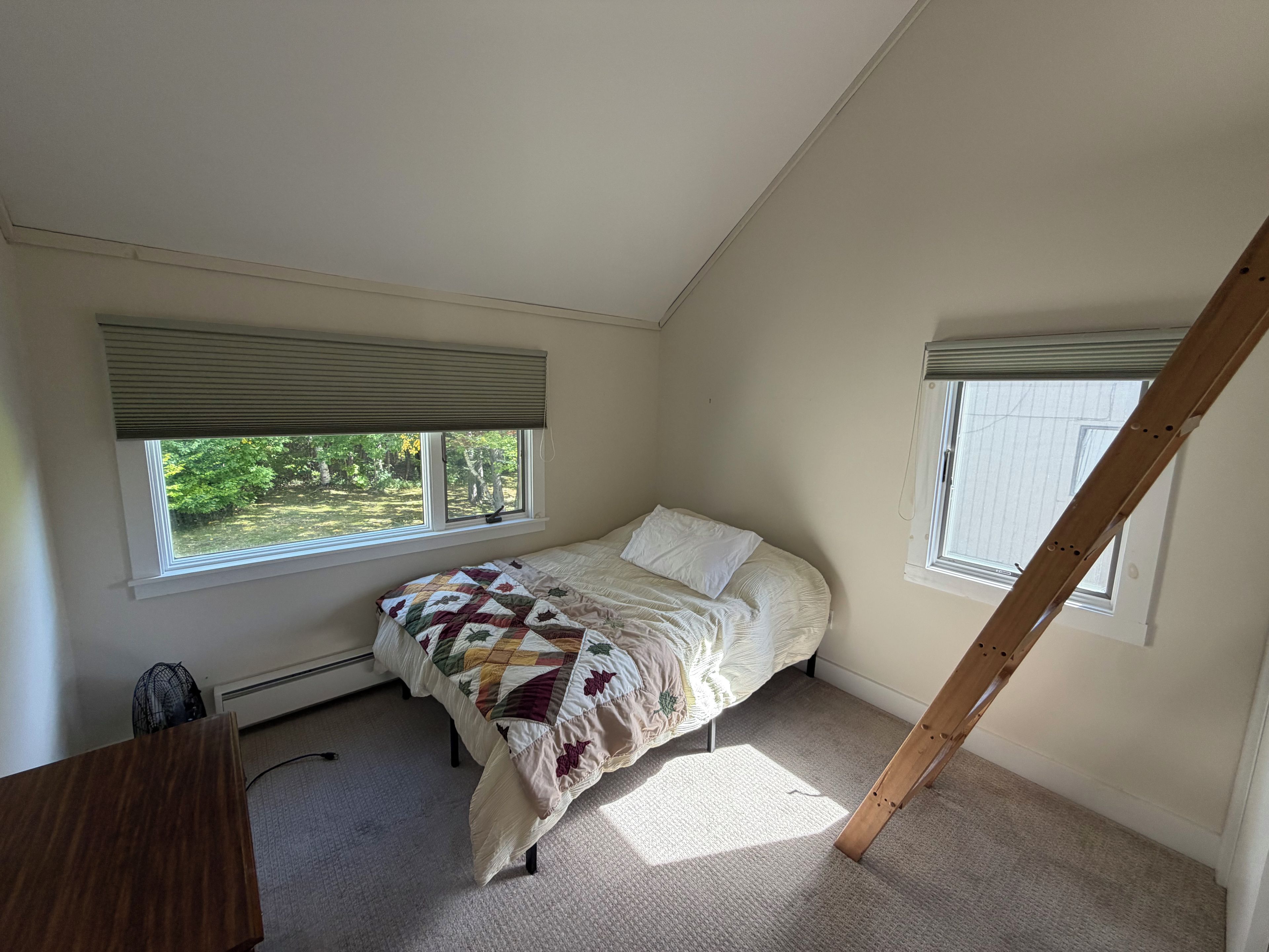Un dormitorio con cama, dos ventanas, un radiador y techo inclinado.