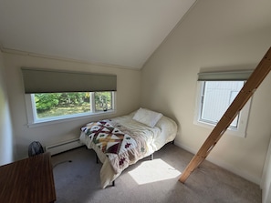 Une chambre à coucher avec un lit, deux fenêtres, un radiateur et un plafond en pente.