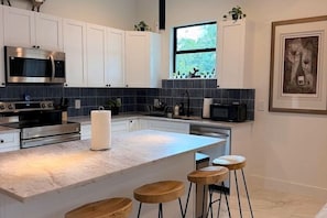 A modern kitchen with white cabinets, a central island with stools, stainless steel appliances, and a window with a view.