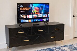 A flat-screen TV on a black TV stand with multiple streaming service icons, a remote control, and a door in the background.