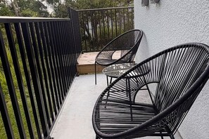 Un balcón con dos sillas de mimbre negro y una mesita.