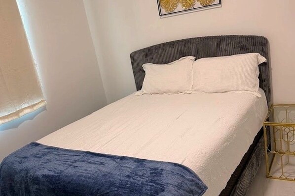 A bed with a white mattress and pillows, a dark headboard, and a blue blanket.