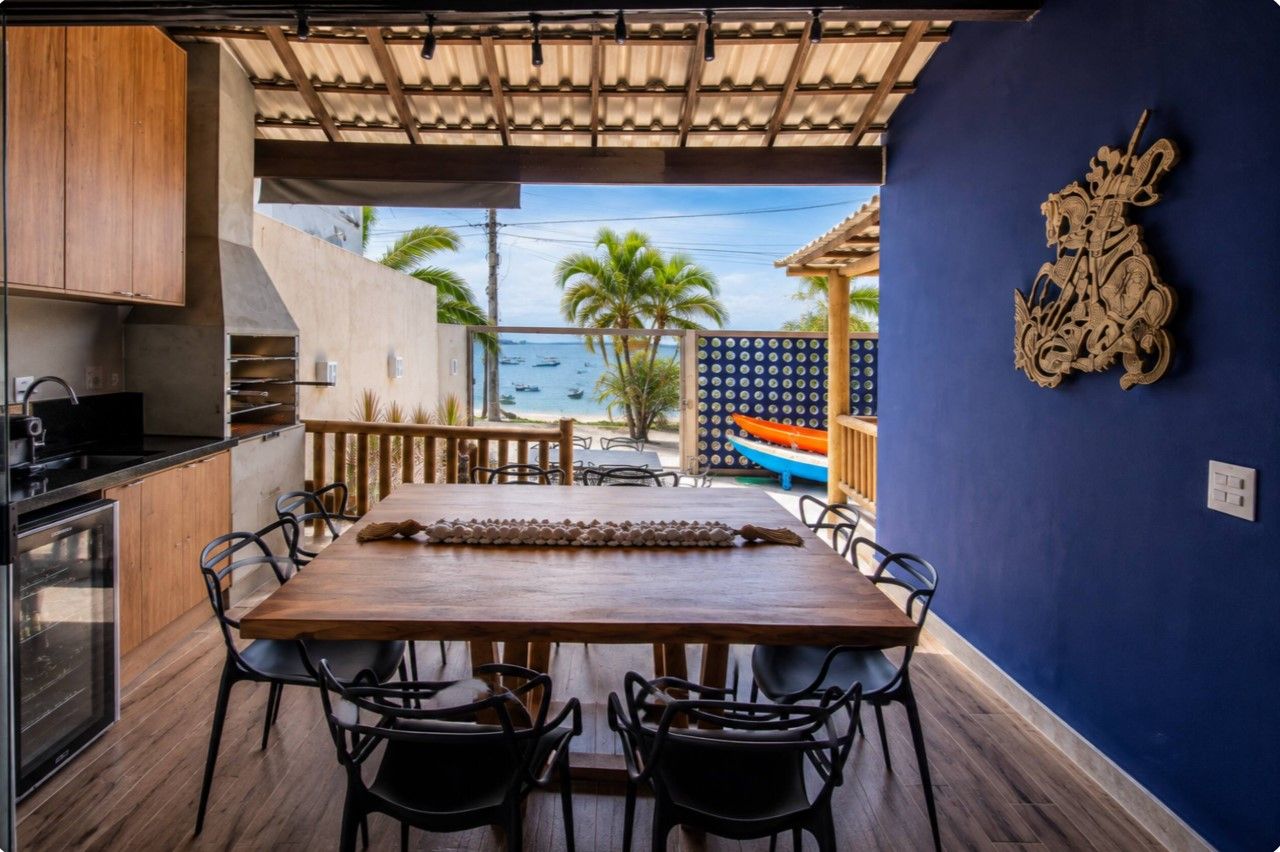 Un área de comedor al aire libre con una mesa y sillas de madera, vista al mar y un elemento decorativo en la pared.