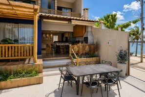 Un'area pranzo esterna moderna con tavolo e sedie, una pergola in legno e vista sul mare.