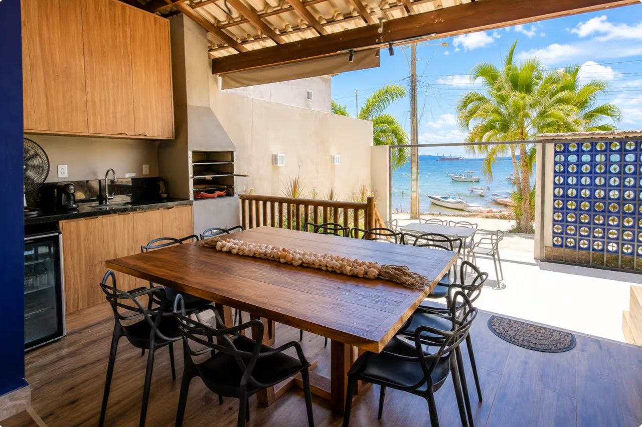 A kitchen with a wooden table and chairs, a fan, and a view of the sea with boats.