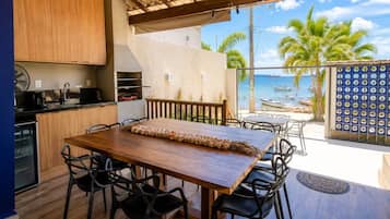 A kitchen with a wooden table and chairs, a fan, and a view of the sea with boats.