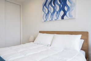 Un lit bien fait, avec une literie blanche, une tête de lit en bois et un tableau abstrait accroché au mur.
