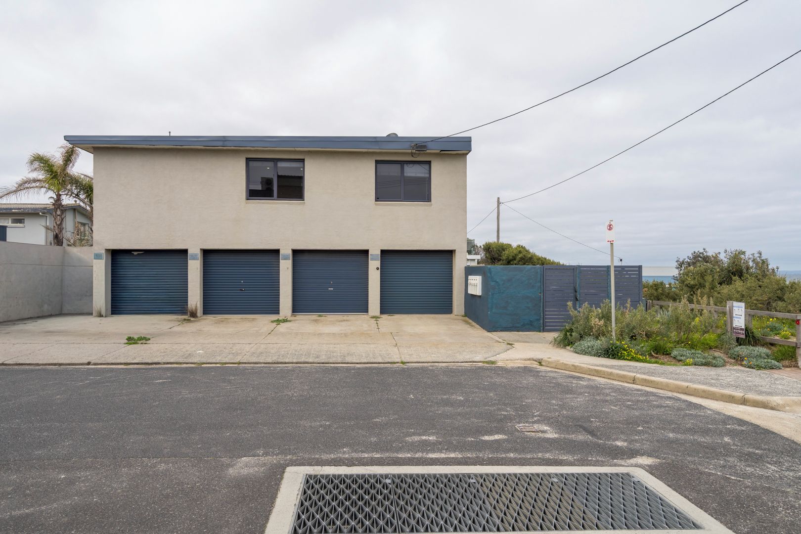 A two-story building with a flat roof, three garage doors, and a gated entrance.