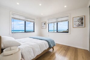 A bedroom with a bed, two windows with ocean views, and a framed picture on the wall.