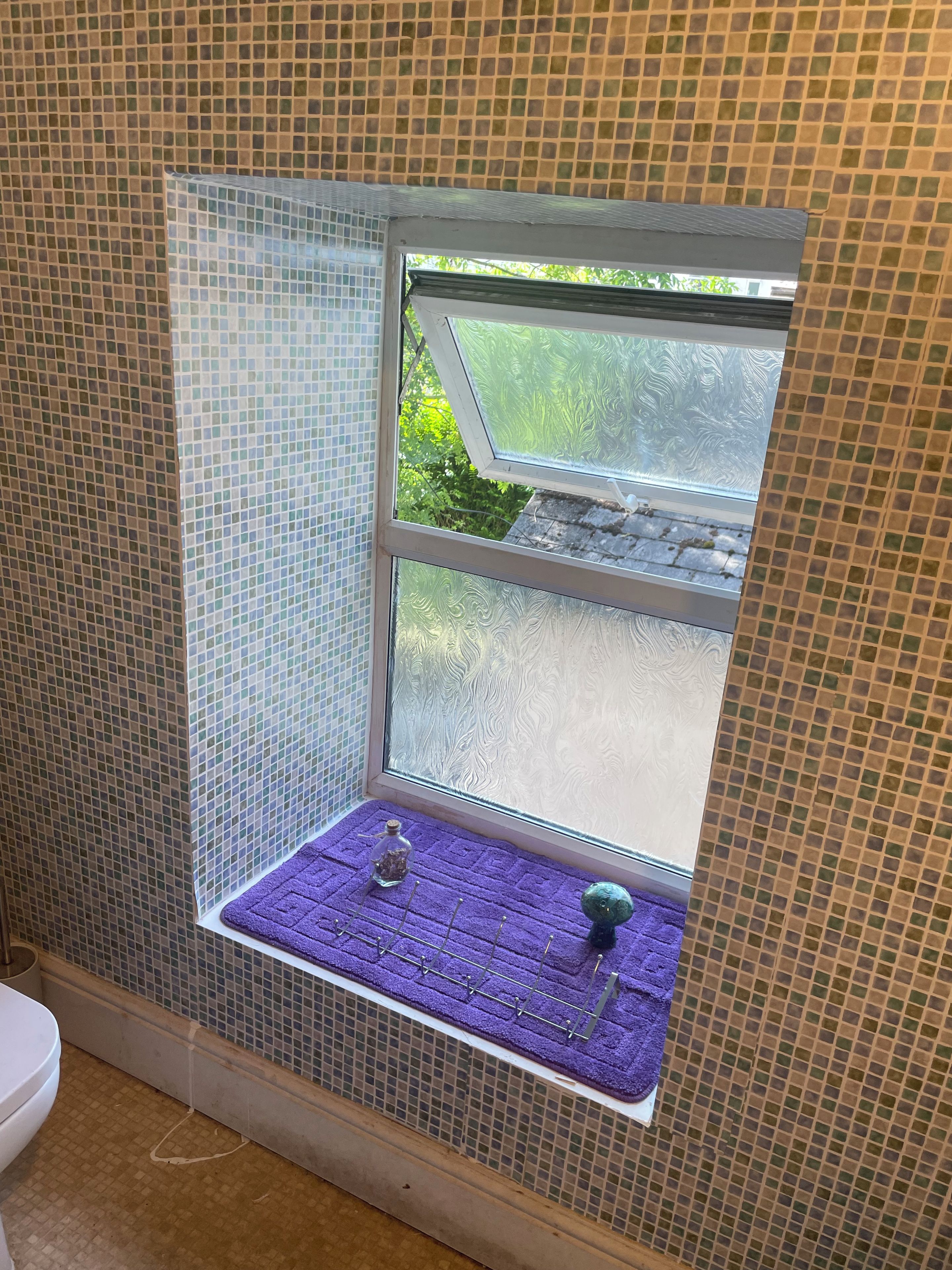 A bathroom with a window, a purple towel rack, and a small shelf with a bottle and a decorative item.
