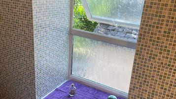 A bathroom with a window, a purple towel rack, and a small shelf with a bottle and a decorative item.