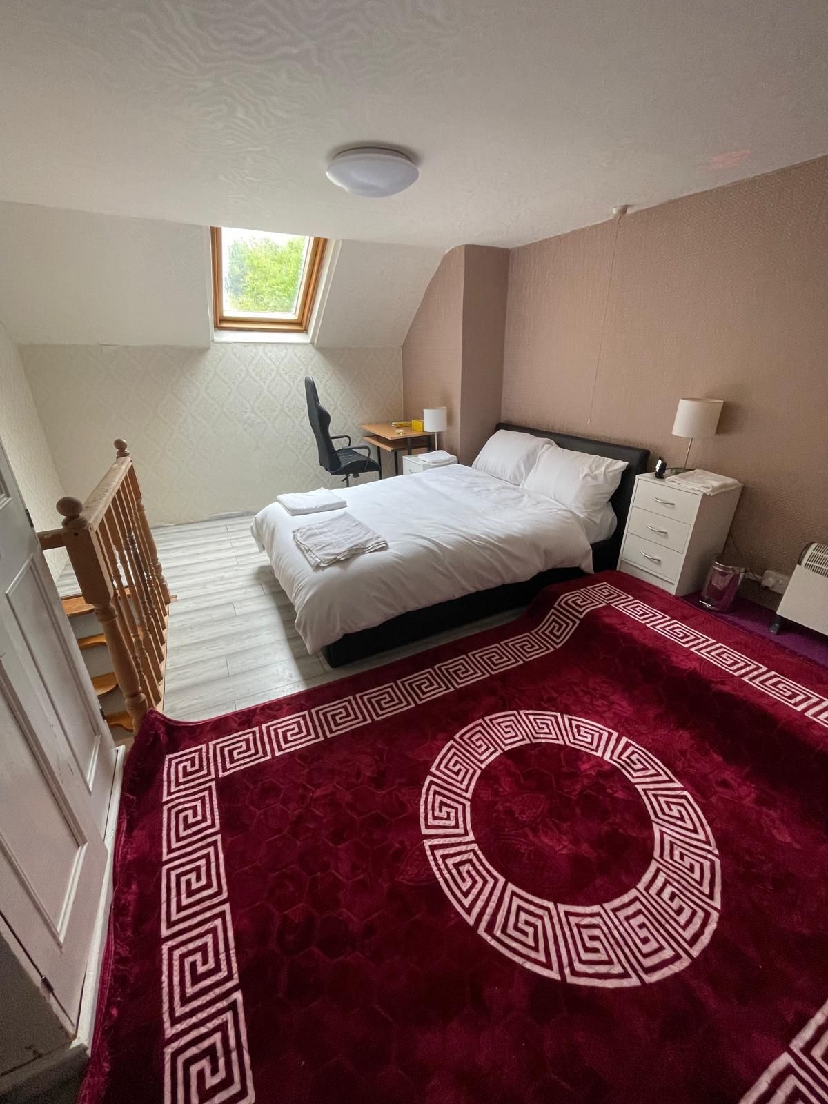 Une chambre à coucher comprenant un lit, un bureau, une chaise, une table de chevet et une fenêtre.