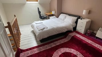 A bedroom with a bed, a desk, a chair, a nightstand, and a window.