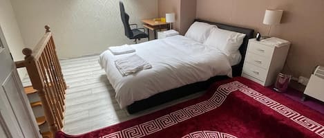 Une chambre à coucher comprenant un lit, un bureau, une chaise, une table de chevet et une fenêtre.