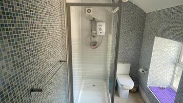Ein Badezimmer mit einer Duschkabine, einer Toilette und einer Badewanne mit einer violetten Matte.