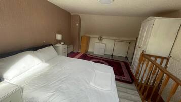 A bedroom with a bed, a nightstand, a dresser, a red patterned rug, a wooden railing, and a ceiling light.