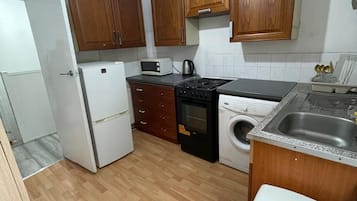 A compact kitchen with wooden cabinets, a refrigerator, a microwave, a stove, a washing machine, and a sink.
