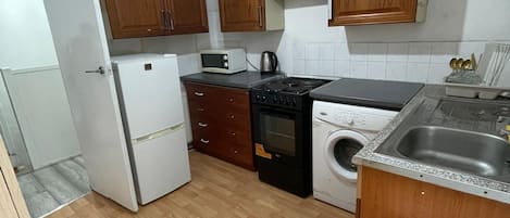 A compact kitchen with wooden cabinets, a refrigerator, a microwave, a stove, a washing machine, and a sink.
