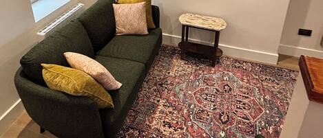 A living room with a green sofa, a patterned rug, and a framed floral artwork on the wall.