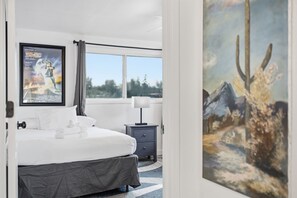 A hotel room with a bed, a nightstand, a lamp, a poster on the wall, and a painting. - Outlaw - Pool - Putting Green - Mins to Old Town (Scottsdale)