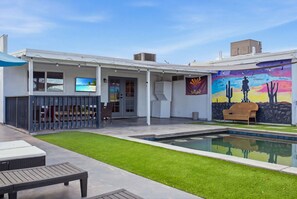 A poolside area with a mural, outdoor seating, and a flat-screen TV. - Outlaw - Pool - Putting Green - Mins to Old Town (Scottsdale)