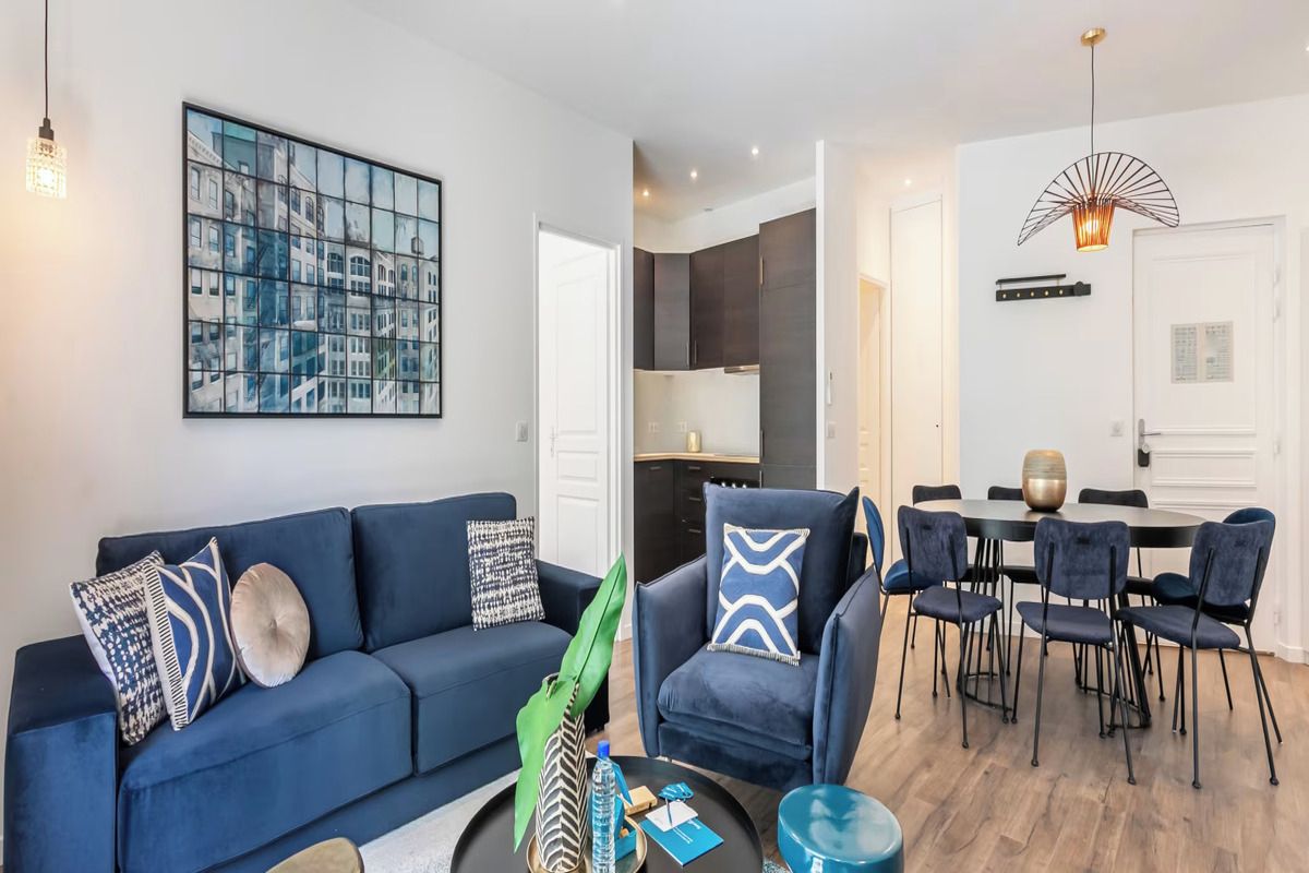 A modern living room with a sofa, armchairs, a dining table with chairs, and a kitchen in the background.